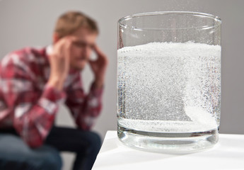Stressed man sitting with head ache migraine near glass of water