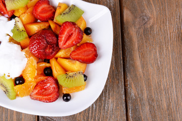 Fresh fruits salad with ice cream on plate on wooden background