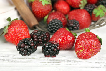 Strawberries and blackberries in metal basket on table close up