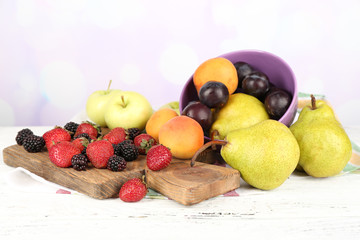 Ripe fruits in bowl and berries on table on bright background