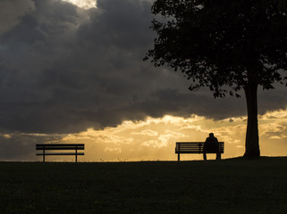 Silhouette of an anonymous man alone on a bench at sunset