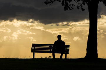 Silhouette of an anonymous male alone on a bench at sunset