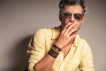 cool fashion man with sunglasses enjoying his cigarette
