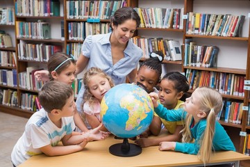 Cute pupils and teacher looking at globe in library