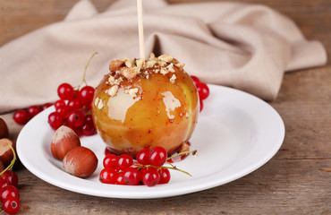 Sweet caramel apple on stick with berries, on wooden table