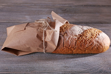 Fresh baked bread wrapped in paper, on wooden background