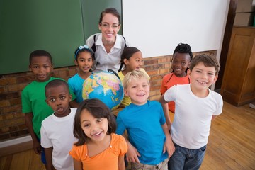 Cute pupils smiling around a globe in classroom with teacher