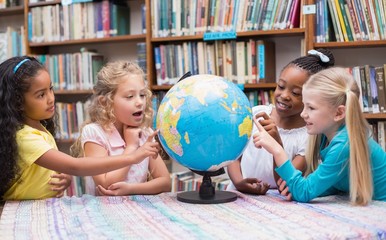 Cute mixed race pupils looking at globe in library