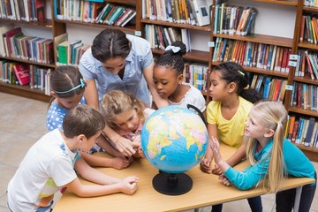 Fototapeta premium Cute pupils and teacher looking at globe in library