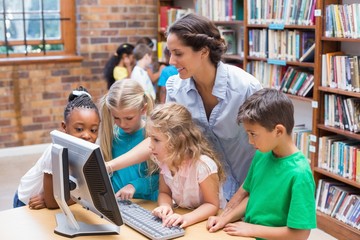 Cute pupils and teacher looking at computer in library