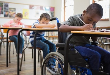 Cute pupils writing at desks in classroom