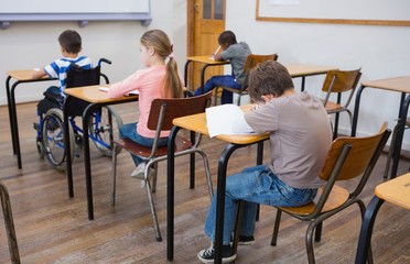 Fototapeta na wymiar Disabled pupil writing at desk in classroom