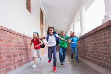 Cute pupils running and smiling at camera in hallway