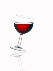 Glass of red wine, tilted, with reflection, white background.