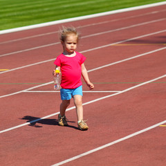 Fototapeta premium Little baby girl carries water in a bottle at the stadium