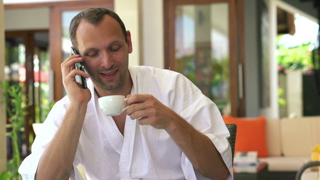 Young man talking on cellphone and drink coffee by the table