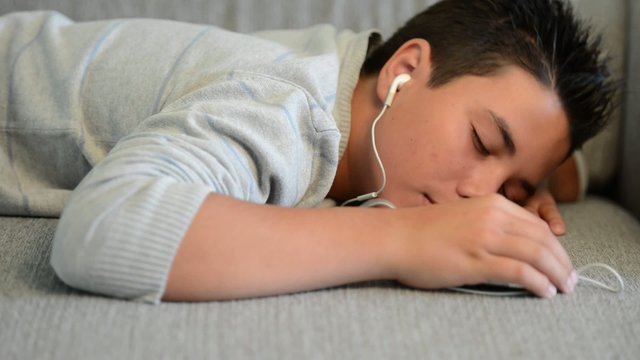 Young teenager sleeping on a sofa listening music on his phone