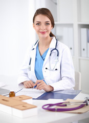 Beautiful young smiling female doctor sitting at the desk and