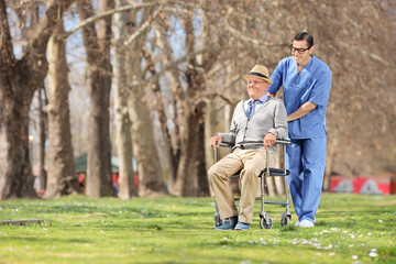 Male nurse pushing a senior in wheelchair outdoors