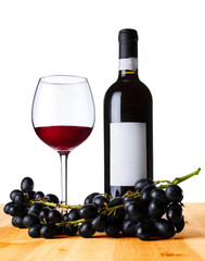 Red wine in the glass and bottle with grape on wood table.