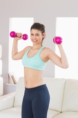 Fit brunette holding dumbbells smiling at camera