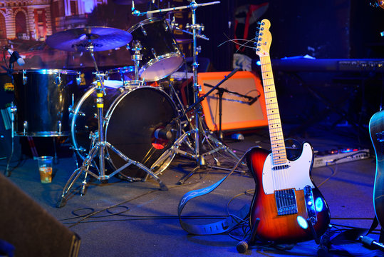 Electric guitar, drum kit, loudspeaker and other musical equipment on stage before concert. Neon light. Concept image. Night club, performance, music band, singing, profession, art, instrument