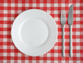 Plate with fork and knife on a red checkered tablecloth.