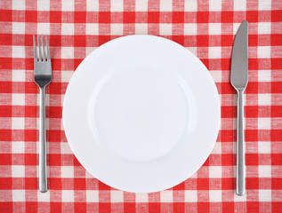 Plate with fork and knife on a red checkered tablecloth.