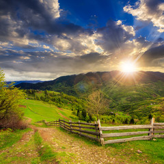 Fototapeta na wymiar fence on hillside meadow in mountain at sunset