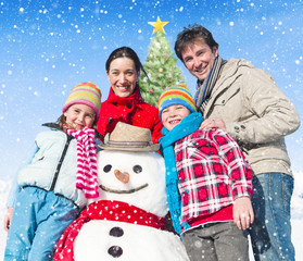 Family Standing Around Snowman And A Christmas Tree Behind Them