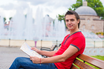 Portrait of young caucasian traveling man reading a map
