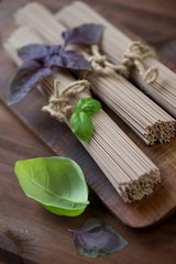 Raw soba noodles with fresh basil leaves, close-up, studio shot