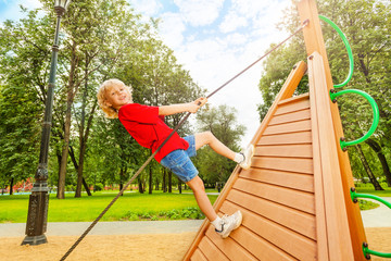 Positive boy climbs on wooden construction