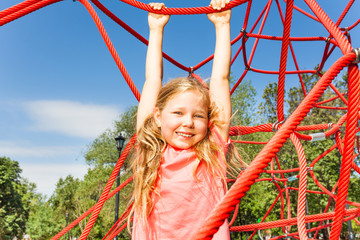 Happy girl hanging on red rope of net outside
