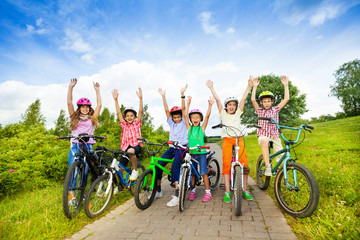 Excited kids in helmets on bikes with hands up