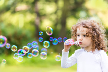 A little girl blowing soap bubbles, closeup portrait beautiful c
