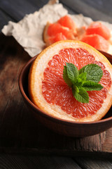 Part of ripe grapefruit in bowl, on wooden background