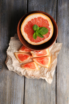 Part of ripe grapefruit in bowl, on wooden background