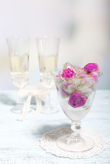 Ice cubes with rose flowers in glass bowl and two glasses with