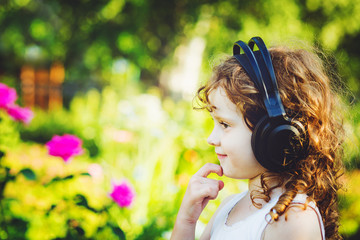 Little girl listening to music on headphones in a summer park