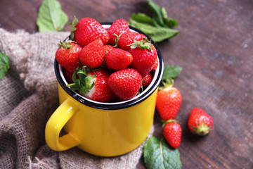 Ripe sweet strawberries in mug  on color wooden background