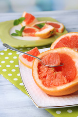 Ripe grapefruits on plate, on wooden table, on light background