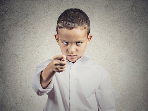Upset boy giving figa gesture with hand, grey wall background 