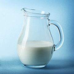 Glass jug of fresh milk on blue background