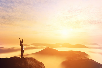 Happy man with hands up on the top of the world above clouds