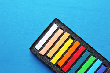 Colorful chalk pastels in box on color wooden background