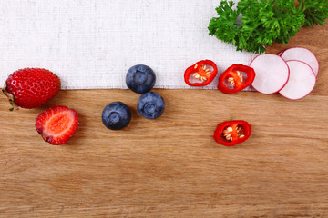 Different slices of vegetables and berries on wooden table