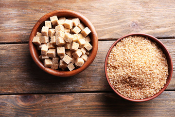 Brown sugar cubes and crystal sugar in bowl on wooden
