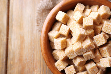 Brown sugar cubes and crystal sugar in bowl on wooden
