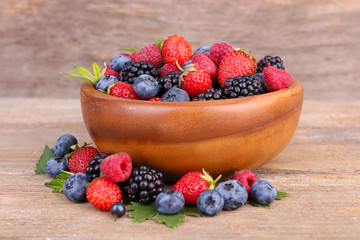 Ripe sweet different berries in bowl, on old wooden table